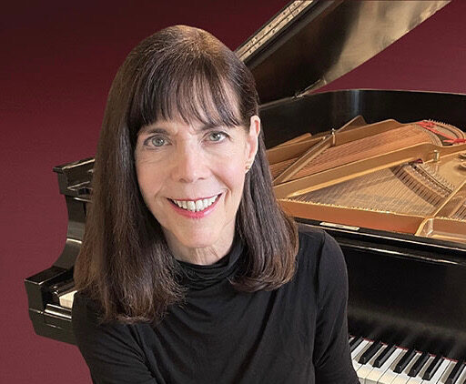 photo of Catherine Rollin wearing black sitting in front of a grand piano with a maroon background
